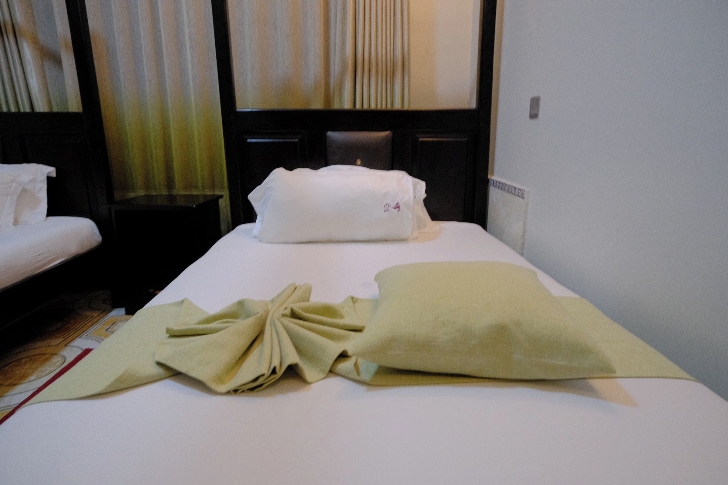 Una habitación de hotel con una cama bien hecha, una mesita de noche y un cabecero con cortinas.
