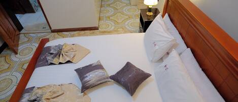 Quarto de hotel com cama, almofadas, mesa de cabeceira com abajur e piso estampado.