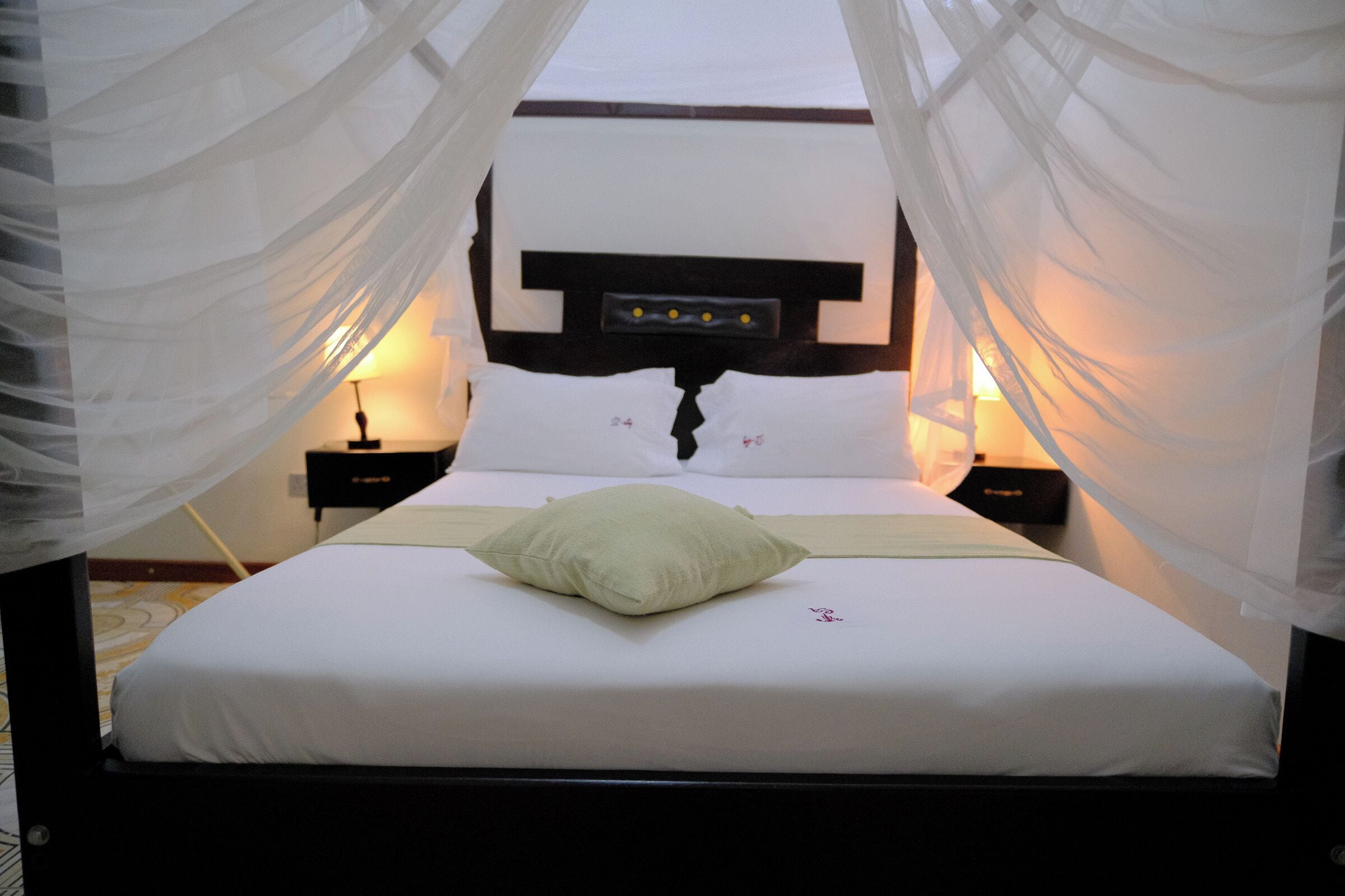Una cama con ropa de cama blanca, un cojín verde y un cabecero con panel de control.