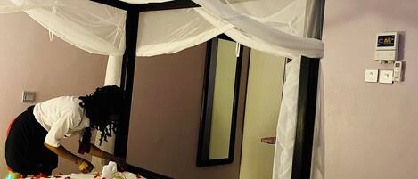 A hotel room with a four-poster bed, an air conditioning unit, a wall-mounted control panel, and a mirror.