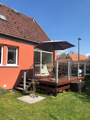 Une maison à l’extérieur rouge, avec une terrasse en bois et un grand parasol.
