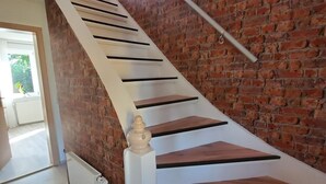Un escalier moderne avec des marches en bois et des rampes blanches, menant à une pièce dotée d’un mur en briques et d’une fenêtre.