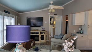 A living room with a sofa, a TV, a ceiling fan, and a table with decorative items. - Private beach access! 2 Bedroom, 2 Full Bath Cottage with many amenities!  (Surfside Beach)