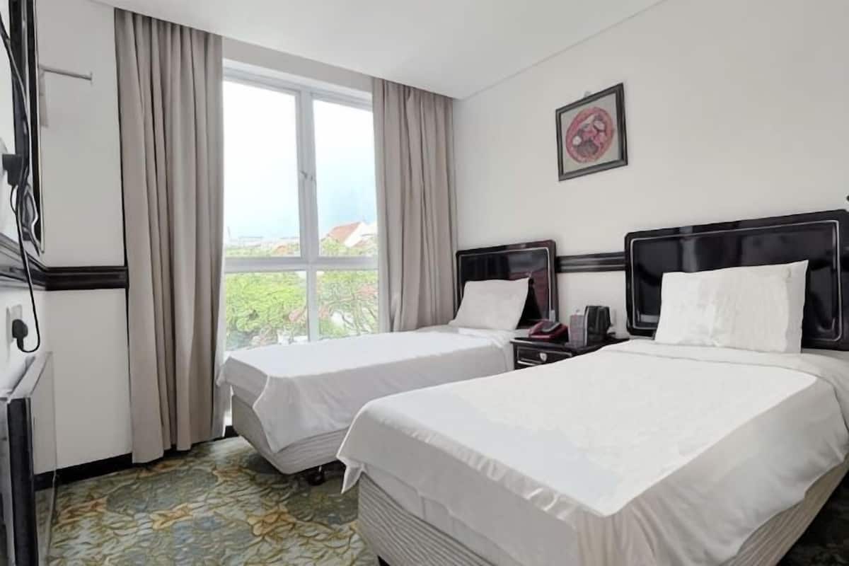 Ein Hotelzimmer mit zwei Betten, einem Schreibtisch, einem Sessel, einem Fernseher und einem Fenster mit Vorhängen.