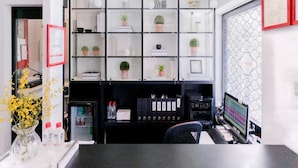 A modern office space with a glass partition, shelves with plants, a desk with a computer, and a red-framed certificate on the wall. - The Snooze Hotel Marine Parade (Singapore)