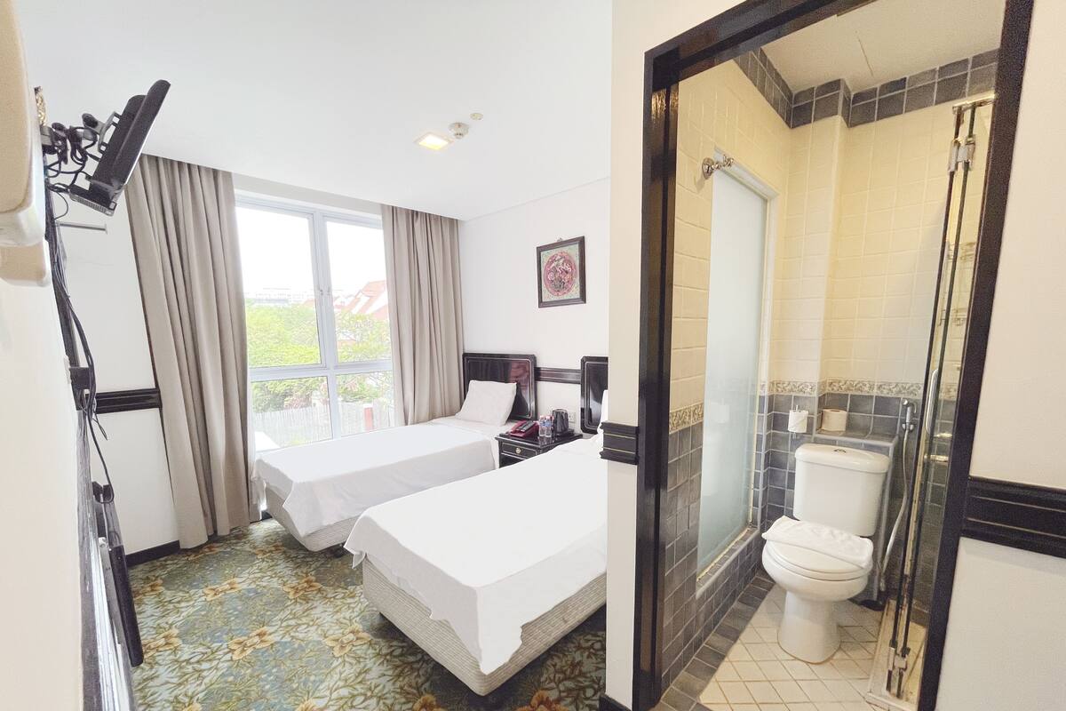Ein Hotelzimmer mit zwei Betten, einem Badezimmer mit Dusche und einem Fenster mit Vorhängen.