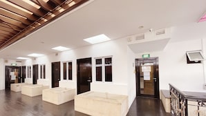 A hotel lobby with a wooden floor, white walls, and multiple doors. There are beige seating areas and a reception desk with a computer monitor. - The Snooze Hotel Marine Parade (Singapore)