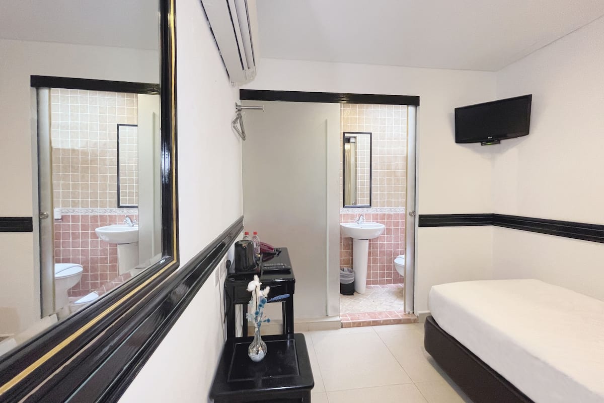 Ein Hotelzimmer mit Bett, Nachttisch, Spiegel, einem an der Wand befestigten Fernseher sowie einem Badezimmer mit Waschbecken und Toilette.