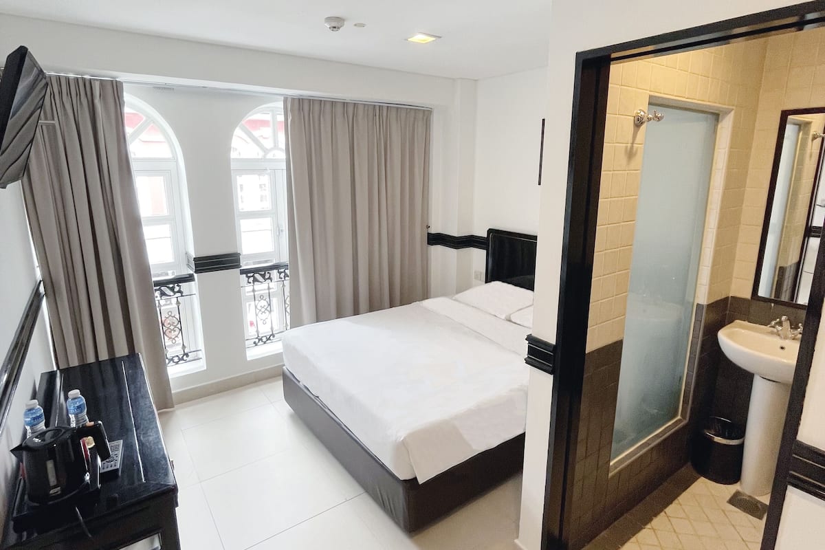 Ein Hotelzimmer mit Bett, Schreibtisch mit Stuhl, Bad mit Waschbecken und Spiegel sowie Blick durch große Fenster nach draußen.