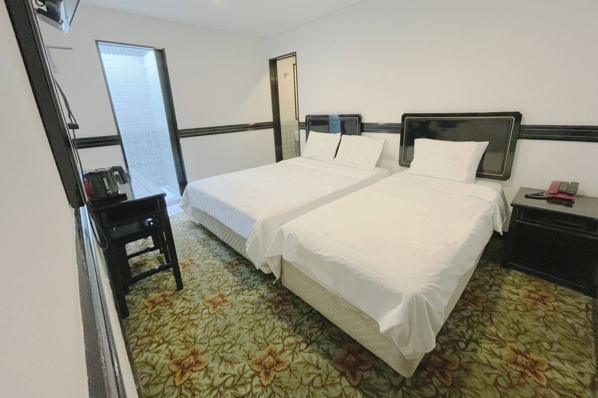 Ein Hotelzimmer mit zwei Betten, einem Schreibtisch, einem Stuhl und einem kleinen Tisch mit Telefon.