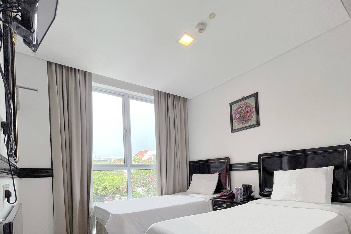 Ein Hotelzimmer mit zwei Betten, einem Schreibtisch, einer Lampe und einem Fenster mit Vorhängen.