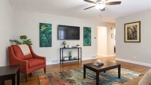 A living room with a red armchair, a coffee table, a TV, and tropical-themed wall art. - *The Comfy King Ranch*King Bed Suite*Fast Wi-Fi (Worth)