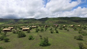 Eine ländliche Landschaft mit einigen kleinen, rustikalen Gebäuden, verstreut auf einer grünen Wiese, umgeben von Hügeln und Bäumen.