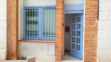 Une entrée d’immeuble avec une porte bleue et une fenêtre ornée de barreaux en métal.