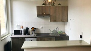Moderni keittiö, jossa on valkoiset laatat, puukaapit, sisäänrakennettu mikroaaltouuni ja pesuallas.