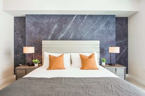 A modern hotel room with a large bed, two nightstands, a marble wall, and two lamps. - Bay & Pool View! Modern 1Bdrm-Miami Design Dist (Miami)