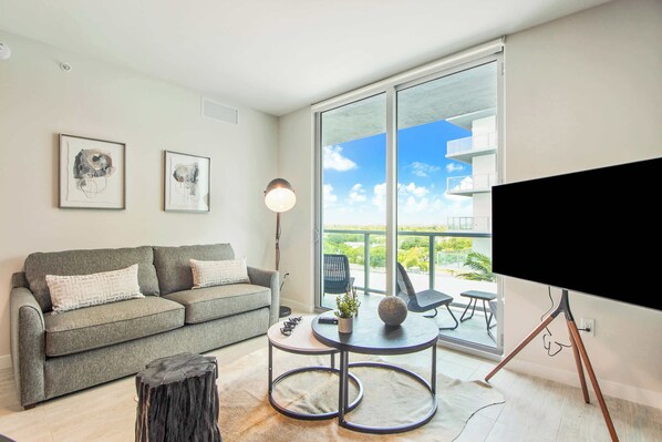 A modern living room with a grey sofa, a round coffee table, and a flat-screen TV on a stand. - Bay & Pool View! Modern 1Bdrm-Miami Design Dist (Miami)
