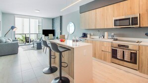 A modern kitchen with a microwave, oven, and bar stools. There is a dining area with a sofa and a table. - Bay & Pool View! Modern 1Bdrm-Miami Design Dist (Miami)