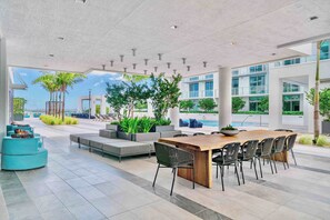 A spacious outdoor area with a long wooden table and chairs, surrounded by modern seating and potted plants. - Bay & Pool View! Modern 1Bdrm-Miami Design Dist (Miami)