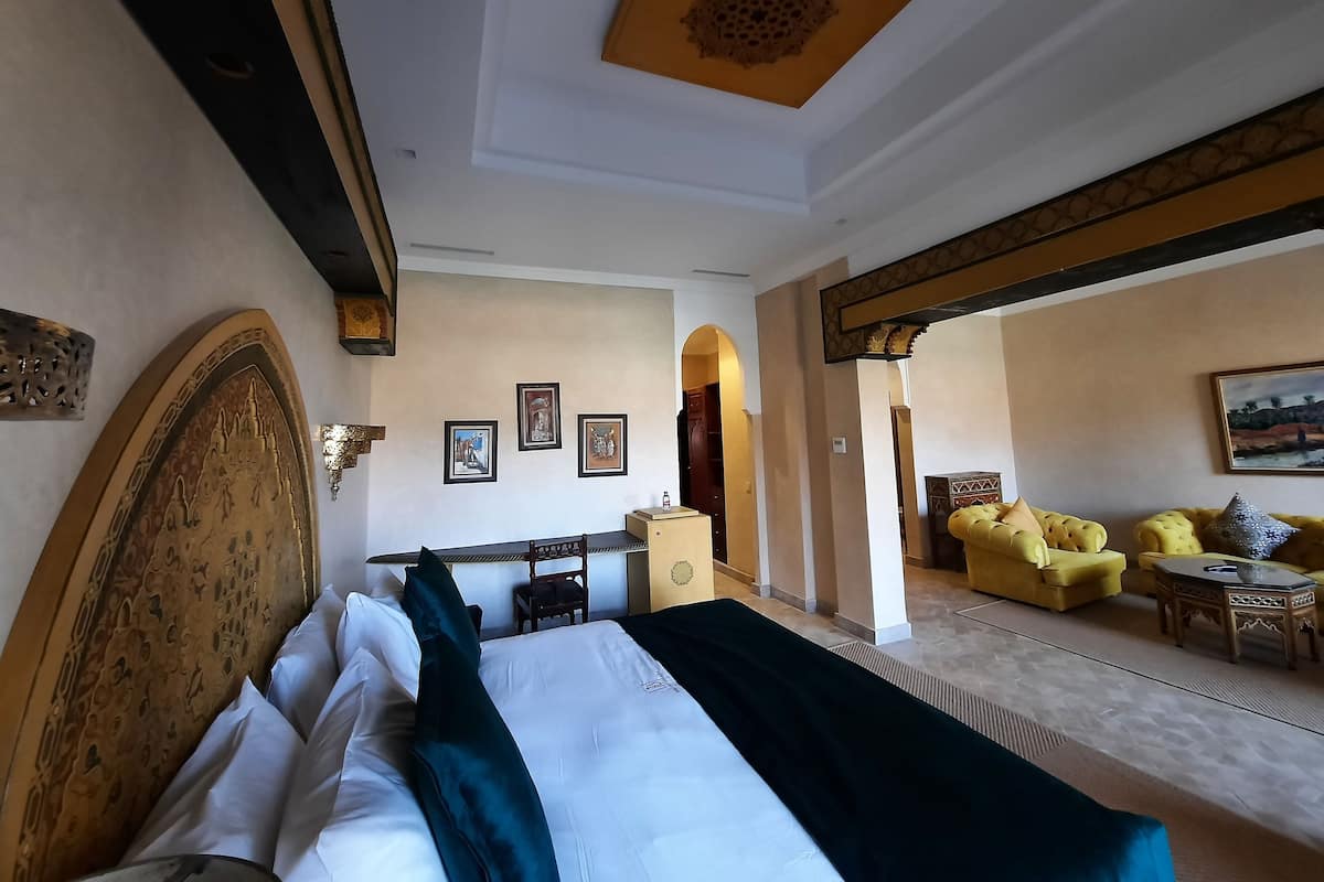 Habitación de hotel con una cama grande, una zona de estar con un sofá amarillo y una zona de comedor con mesa y sillas.