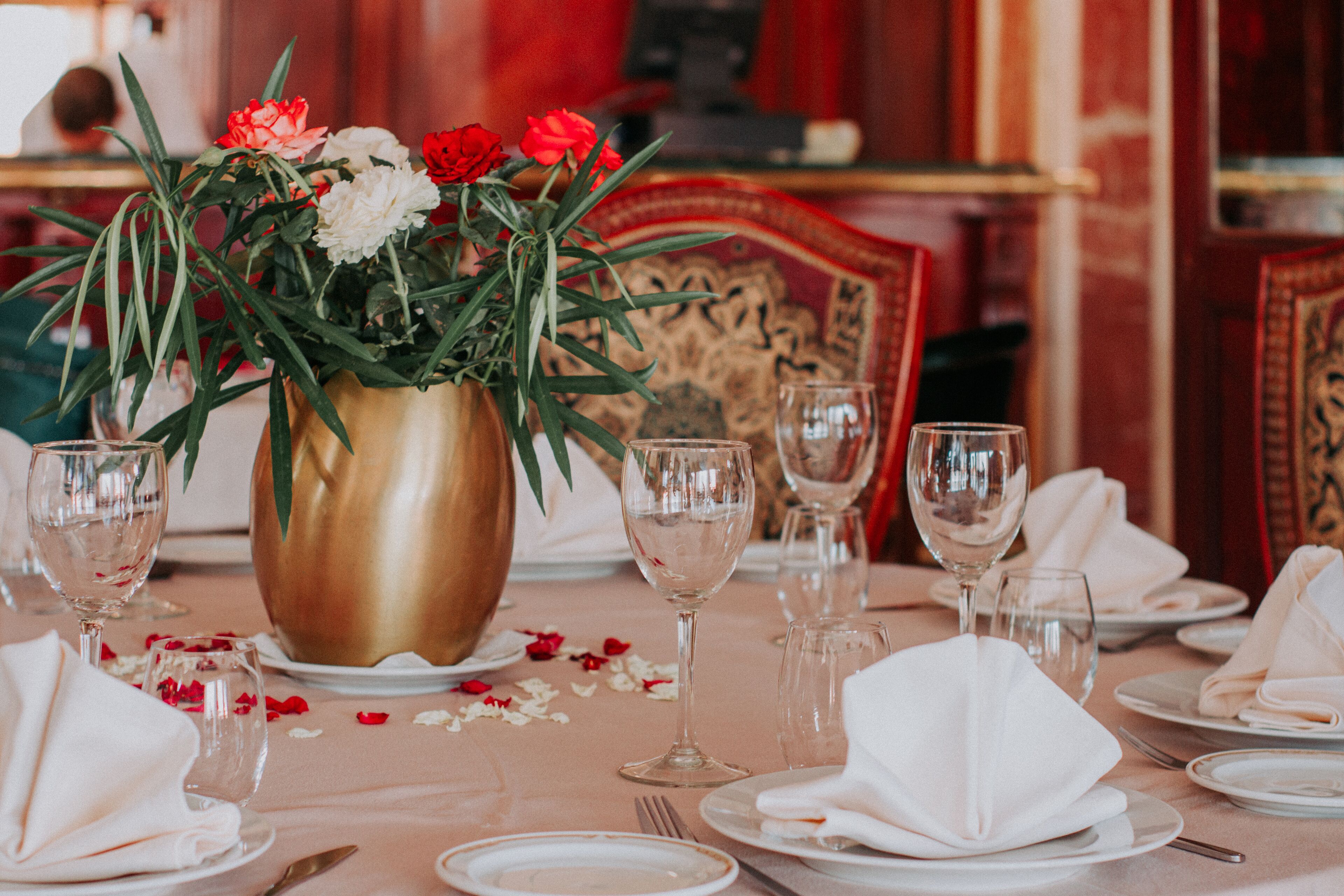 Une table dressée pour un repas formel, agrémentée d’un vase doré rempli de fleurs, de serviettes blanches et de verres à vin vides.