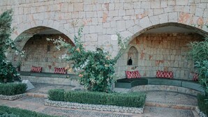A courtyard with stone walls, a bench with red and white patterned cushions, and a small statue. - Borj Des Cascades (Ait Taguella)