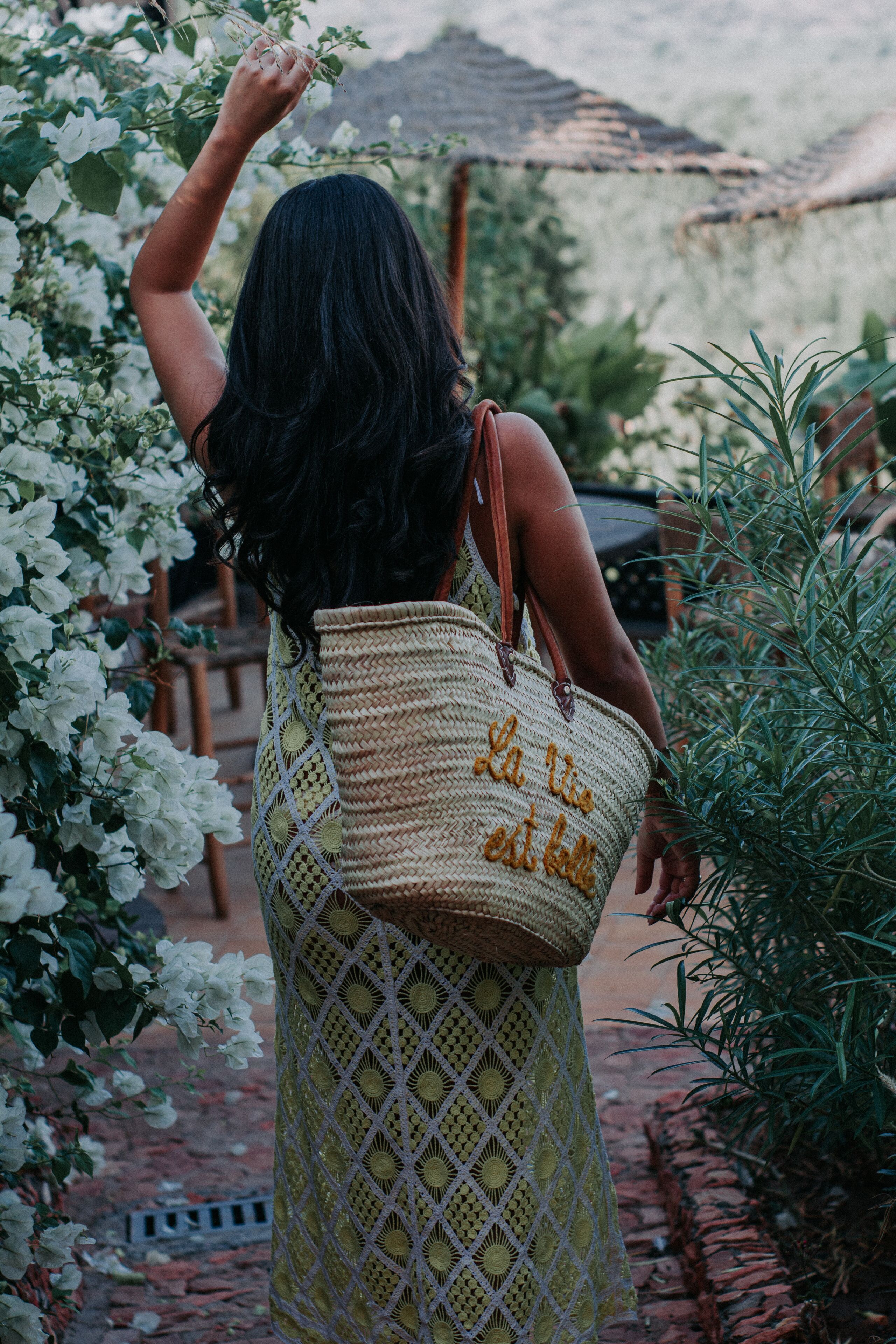 Una persona con un vestido estampado y llevando un bolso tejido con texto.