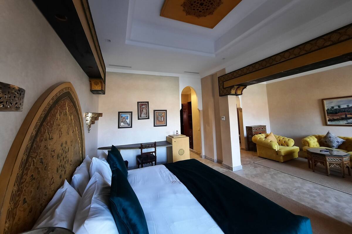Una habitación de hotel con una cama grande, una zona de estar con un sofá amarillo y un comedor con mesa y sillas.