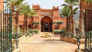 A courtyard with a central fountain, palm trees, and a building with an arched entrance. - Borj Des Cascades (Ait Taguella)