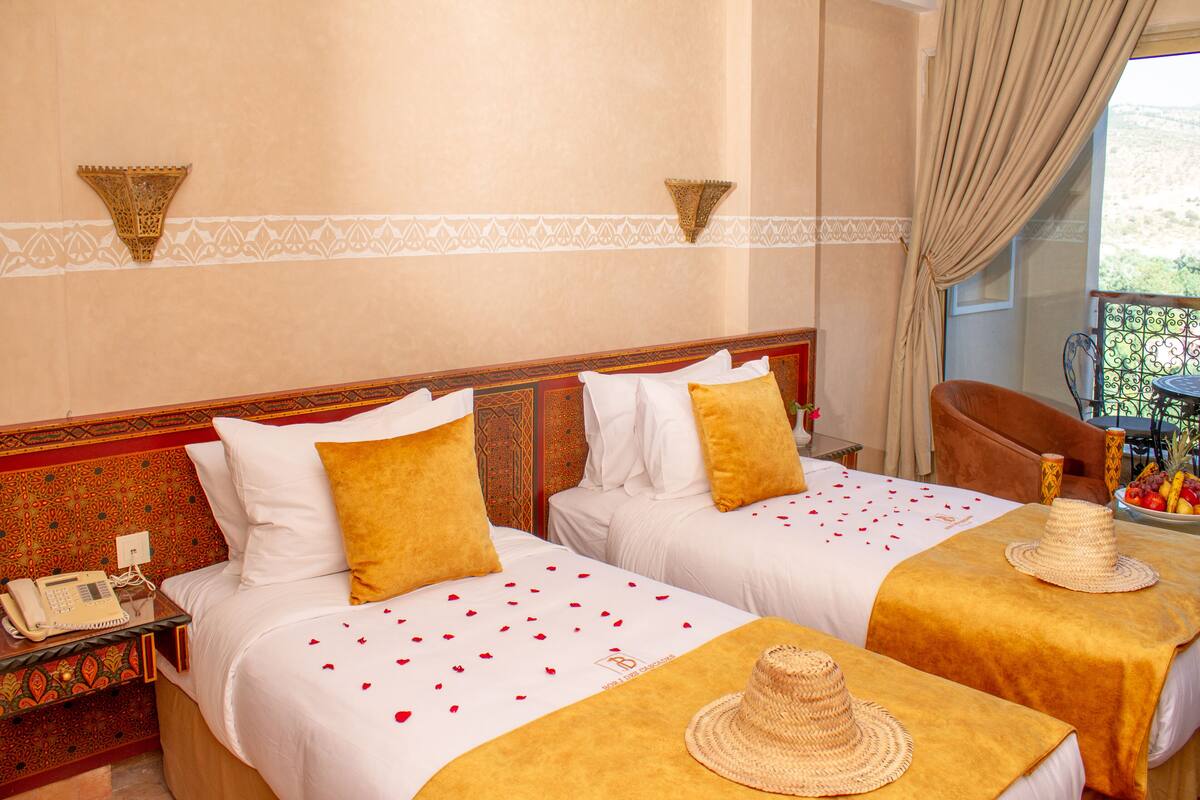 Habitación de hotel con dos camas, una mesita con frutero, teléfono y una silla.
