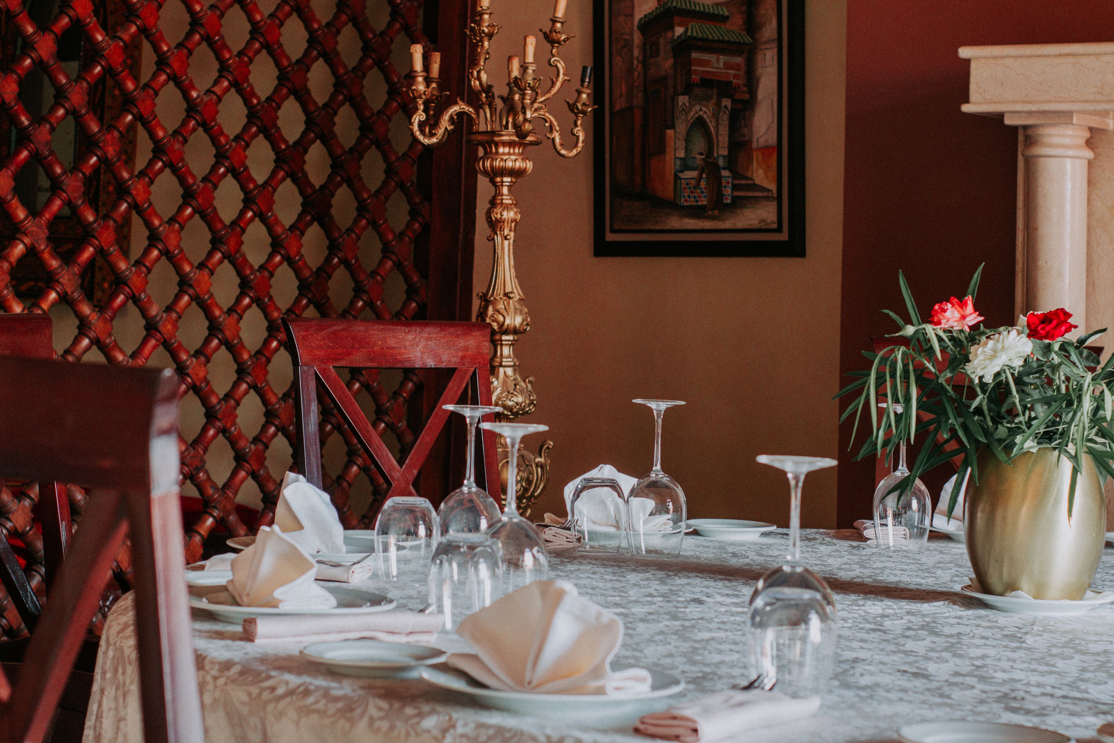 Une table à manger dressée avec de la vaisselle et des verres blancs, un vase rempli de fleurs et un chandelier.