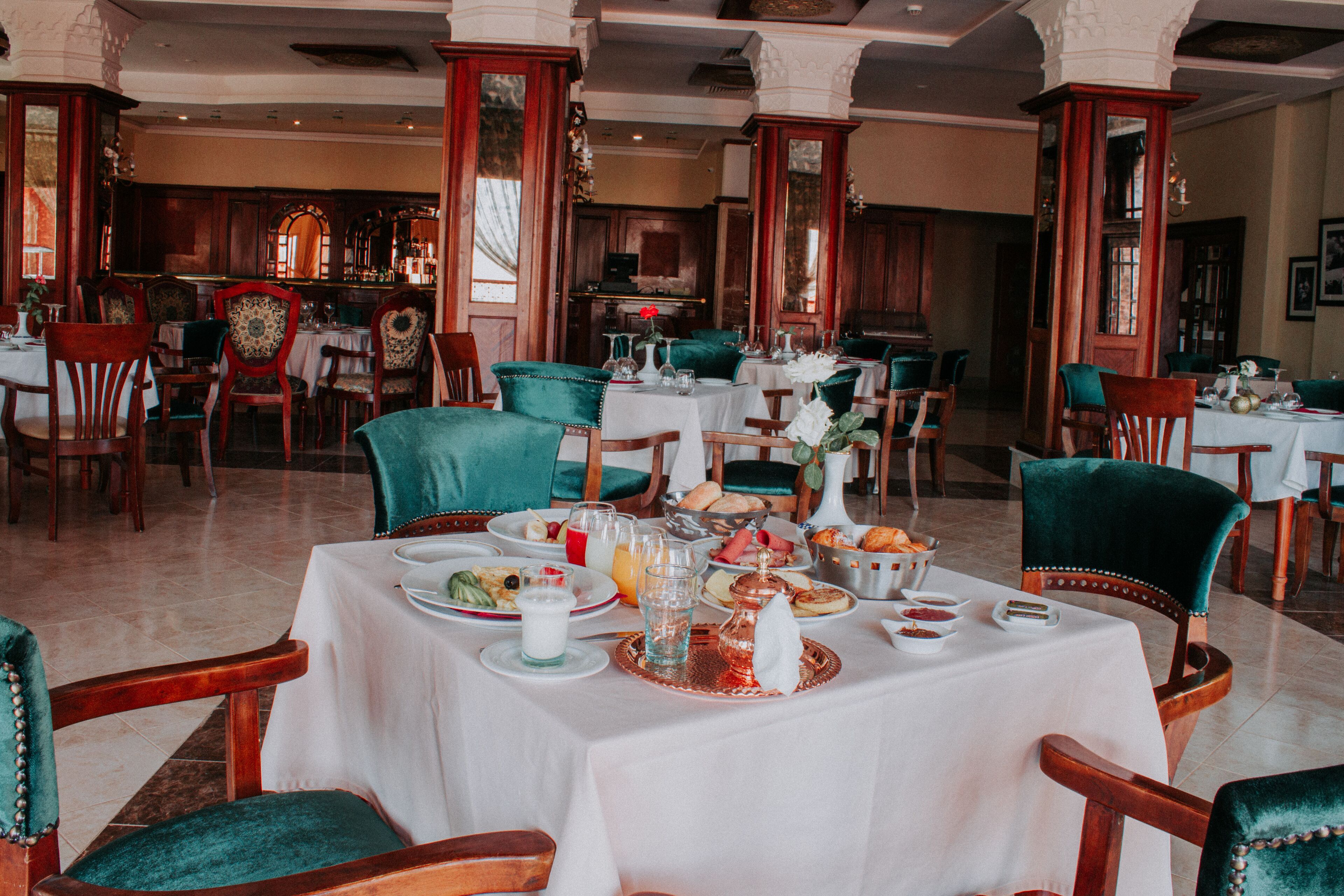 Un restaurante con varias mesas dispuestas para comer, con una decoración clásica que incluye muebles de madera y sillas tapizadas en verde.