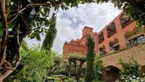 A courtyard with a well-manicured garden, a stone bridge, and a large building with a tower. - Borj Des Cascades (Ait Taguella)
