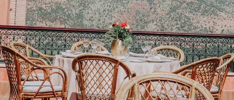 A table set for six with wicker chairs, a vase with flowers, and a mountain view in the background.