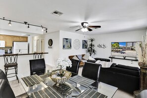 Una sala de estar moderna con una mesa de comedor de cristal, sofás de cuero negro y un ventilador de techo.
