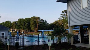 A swimming pool area with a fenced pool, lounge chairs, and umbrellas. There is a sign indicating reserved parking and a handicap parking sign. - Effy's Sunset Serenity Hideaway (Sunset Beach)