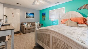 A bedroom with a bed, a ceiling fan, a window with blinds, a couch, and a door. - Effy's Sunset Serenity Hideaway (Sunset Beach)
