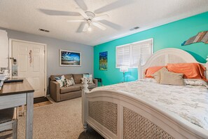A bedroom with a bed, a ceiling fan, a window with blinds, a couch, and a door. - Effy's Sunset Serenity Hideaway (Sunset Beach)