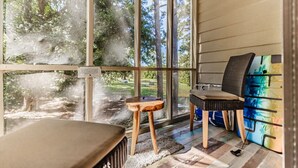 A room with large windows, a small wooden stool, a chair, and a colorful cabinet. - Effy's Sunset Serenity Hideaway (Sunset Beach)