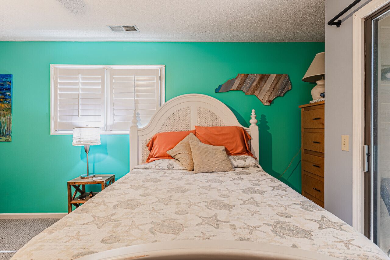 A bedroom with a bed, a window, a dresser, and a lamp.