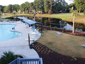 A pool area with lounge chairs and umbrellas, a pond, and a golf course in the background. - Effy's Sunset Serenity Hideaway (Sunset Beach)