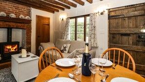 Un comedor acogedor con una mesa de madera dispuesta para cuatro personas, una chimenea y vistas al exterior a través de una ventana con cortinas.