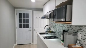 A modern kitchen with white cabinetry, a stainless steel microwave, and a tiled backsplash. - A Lovely Modern Retreat for Your Perfect Stay (Hayward)