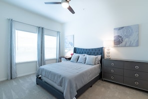 A bedroom with a bed, a nightstand, a dresser, a ceiling fan, and a window with curtains.