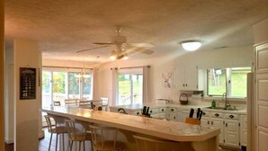 Een keuken met een centraal eiland, barkrukken, een plafondventilator en uitzicht op de omgeving.