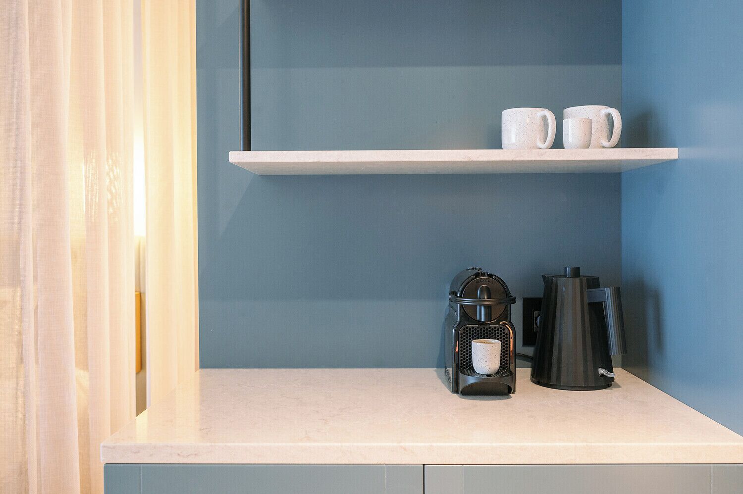 A kitchen counter with a coffee maker, a kettle, and two white mugs on a shelf.