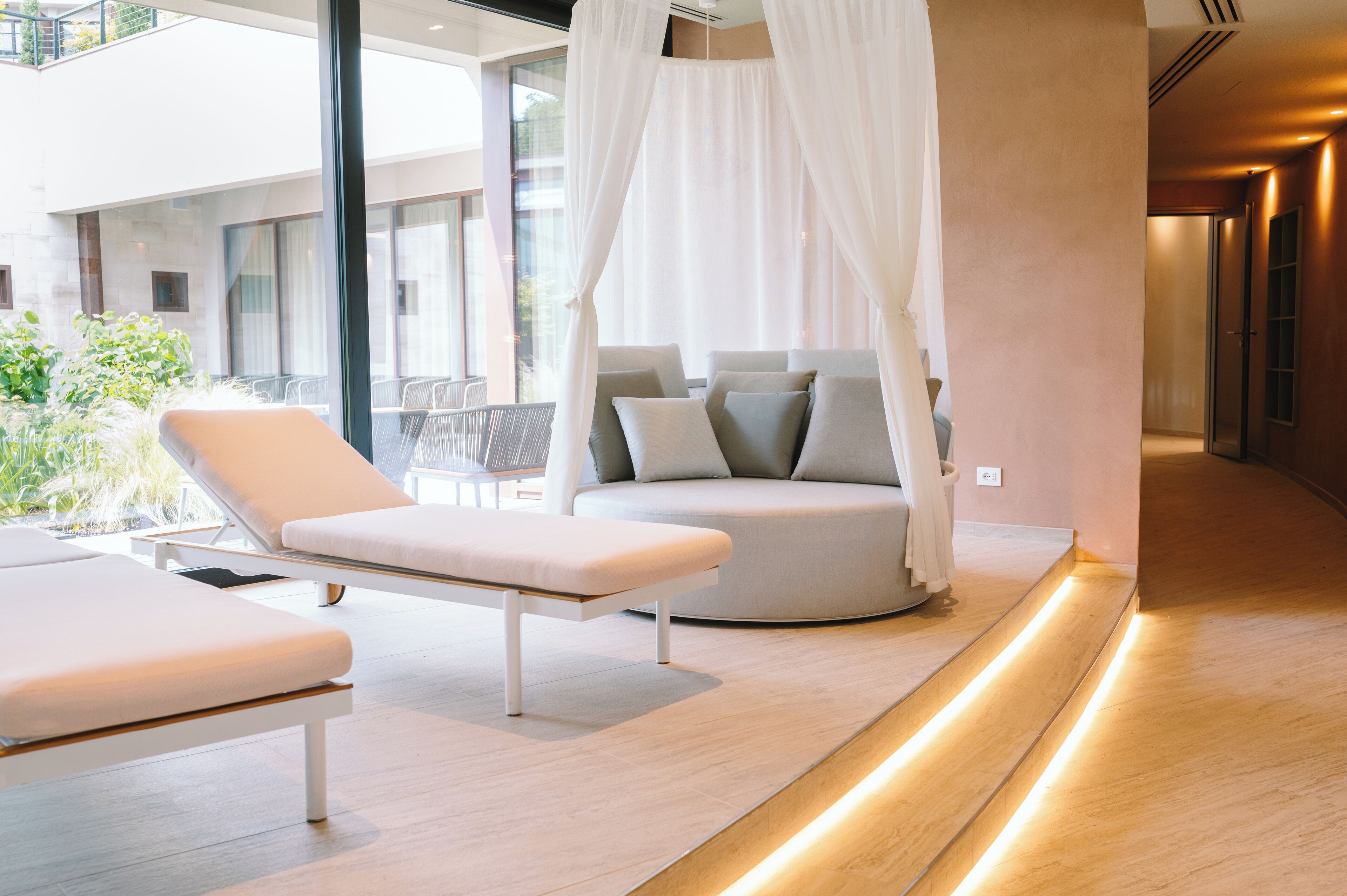 A modern spa room with a white cushioned bench, a round seating area with cushions, and a canopy.