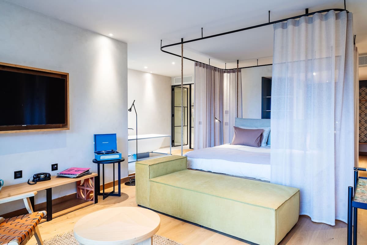 A modern hotel room with a bed, a desk, a chair, a sofa, and a TV.
