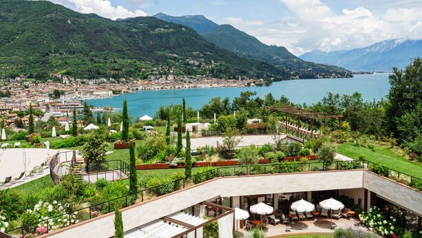 A hotel with outdoor seating overlooking a lake and mountains. - A-ROSA Gardasee (Salò)