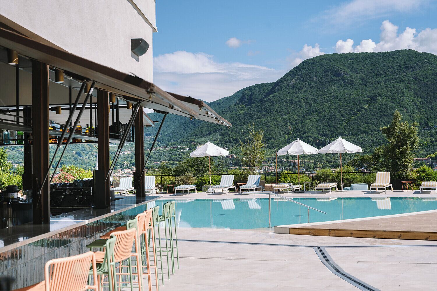A poolside area with lounge chairs and umbrellas, overlooking a mountainous landscape.